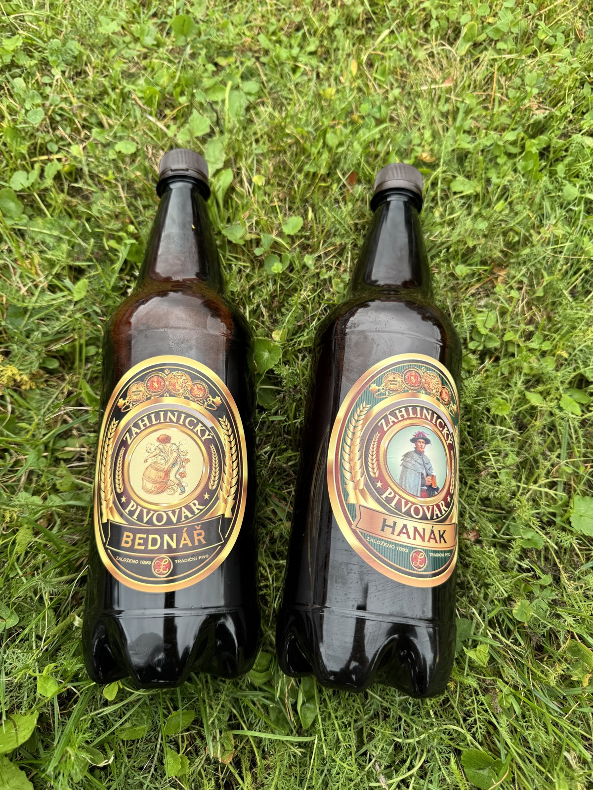 Lahve piva Bednář a Hanák z pivovaru Záhlinice položené na trávě