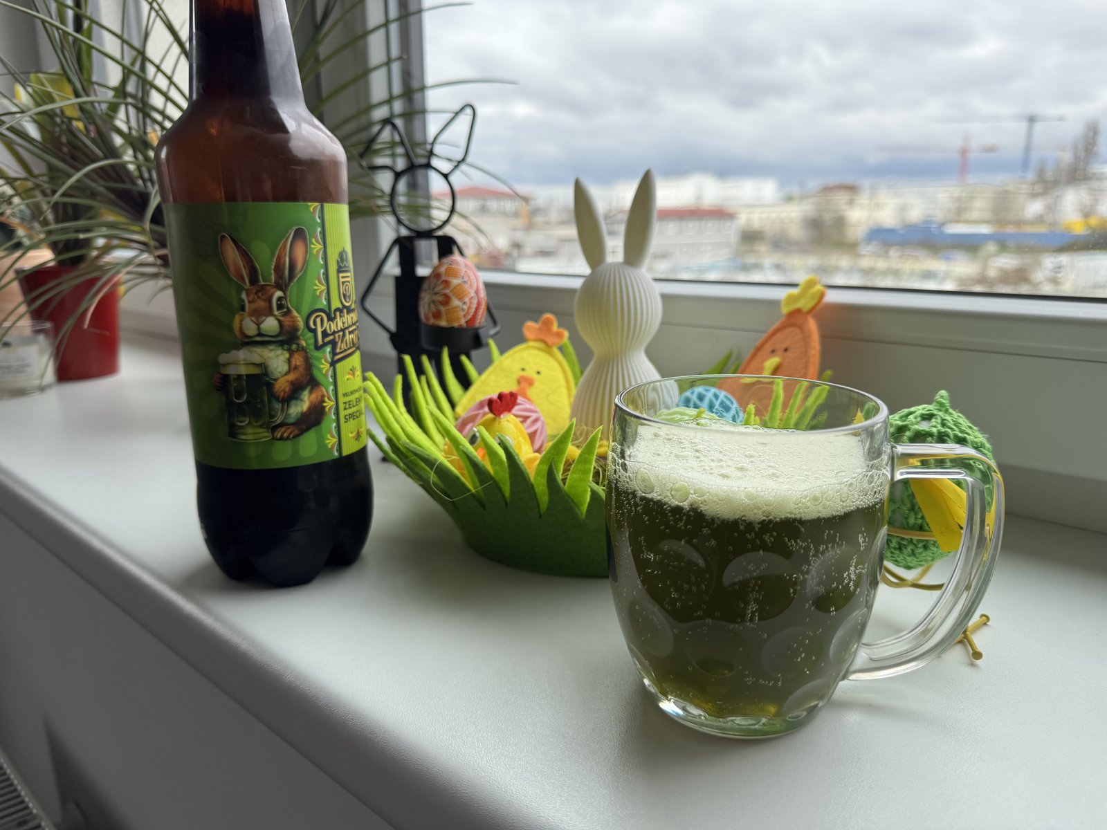 Zelené velikonoční pivo ve sklenici na parapetu s velikonoční dekorací