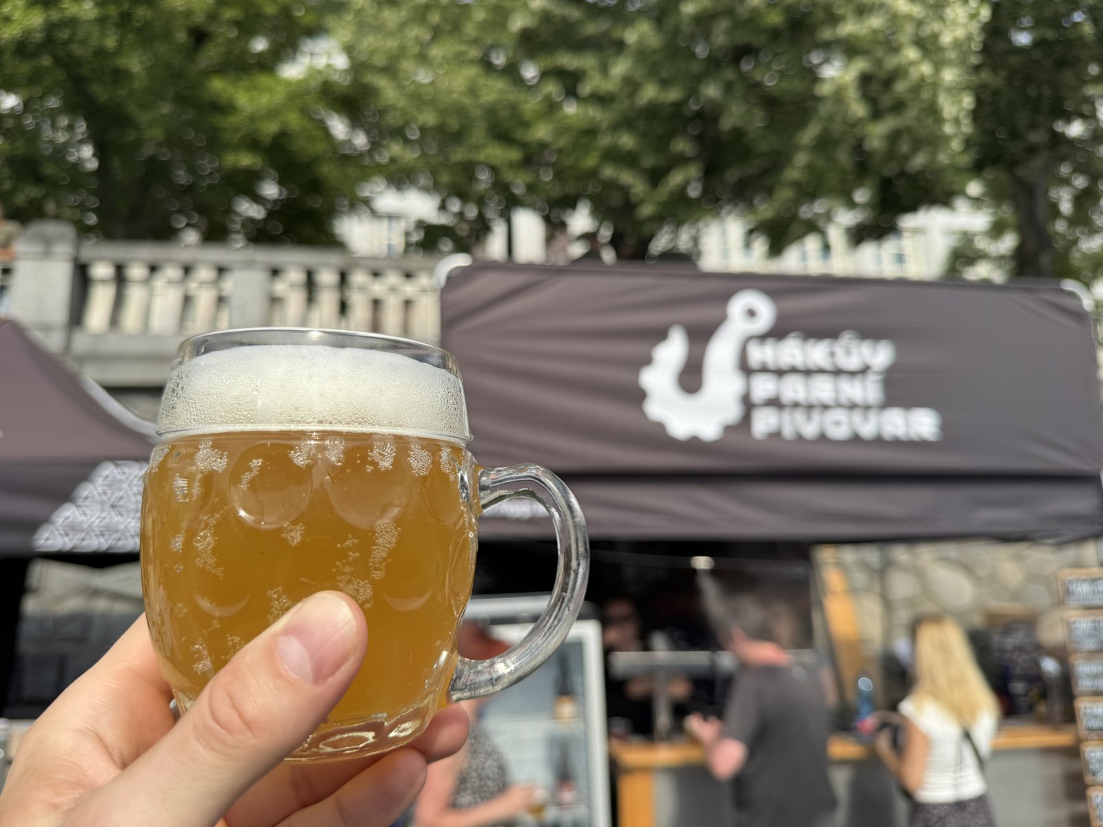 Sklenice piva Bandita od Hákova parního pivovaru před stánkem na festivalu Pivo na Náplavce.