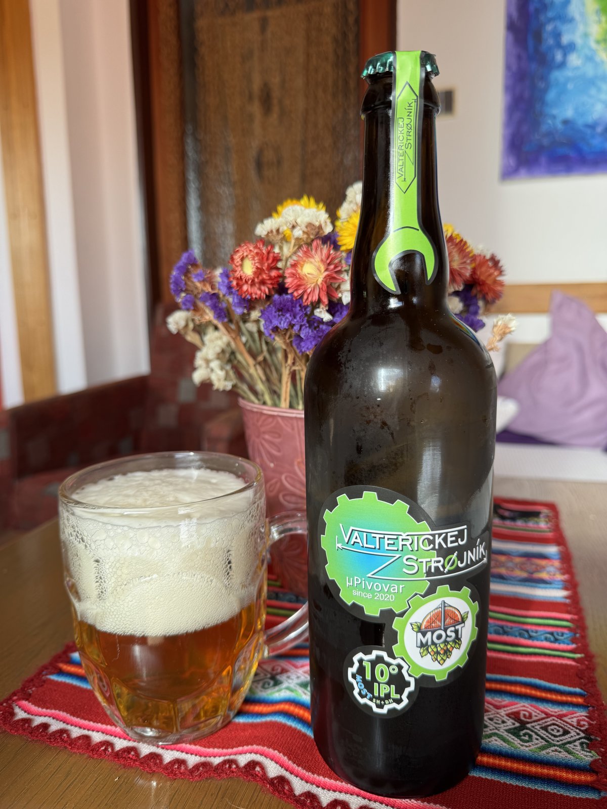 Láhev piva Valteřickej Strojník 10° IPL a načepované pivo ve sklenici na stole.