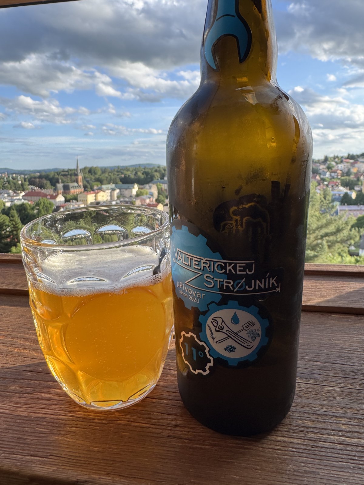 Pivo Valteřickej Strojník 11° ve sklenici s výhledem na město a okolní krajinu.